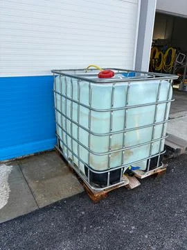 A large intermediate bulk container filled with liquid sits outside a facility Stock Photos