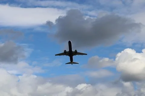 A large jet flying through a cloudy blue sky Stock Photos