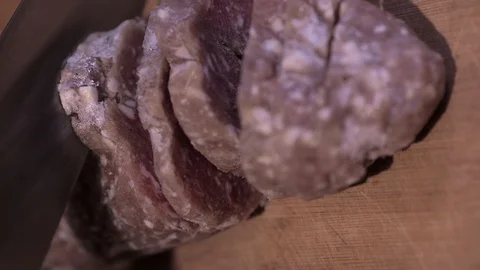 Large kitchen knife, cuts a roll of frozen minced meat, on a wooden Board Stock Footage 129731684