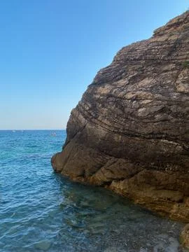 Large, layered rock cliff rises from the clear blue waters of the Adriatic Sea Stock Photos