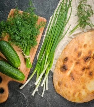A large loaf of bread with green onions and dill on a black background. Stock Photos