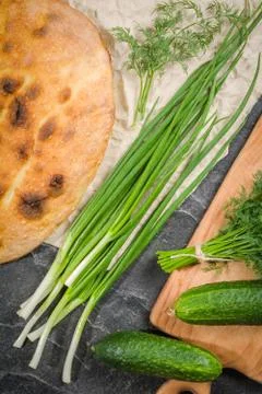 A large loaf of bread with green onions and dill on a black background. Stock Photos