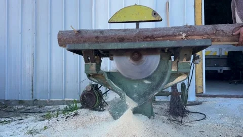 Large log being cut on table saw with exposed blade, hand feeding wood 스톡 동영상 326037133