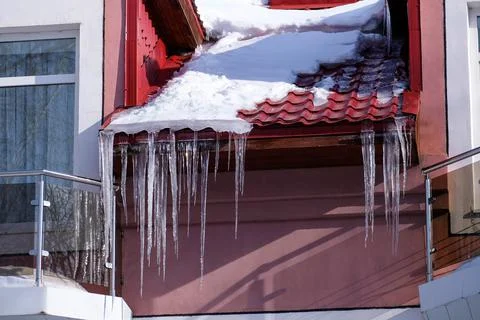 Large long icicles hang under the roof of the building Stock Photos