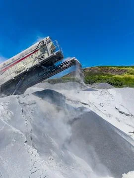Large machine moves granite material from the ground to a waiting truck in a  Stockfoto's