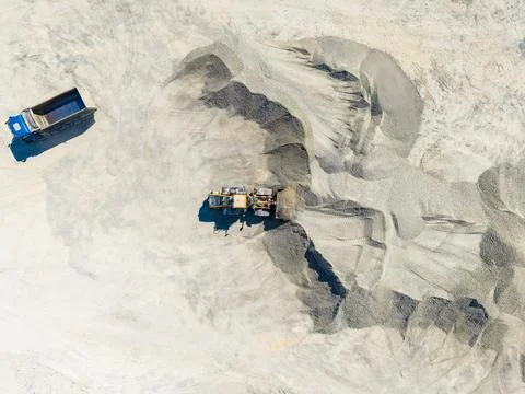 A large machine moves materials at a granite quarry while a dump truck waits  Foto stock