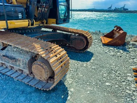A large machine with tracks sits on rocky ground near the water. Metal parts  Fotos Stock