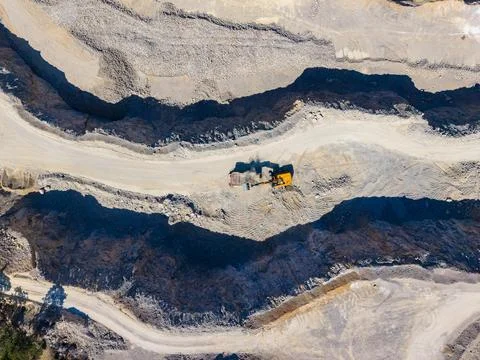 A large machine works in a mine, moving dirt and rocks. The landscape shows l Stock Photos