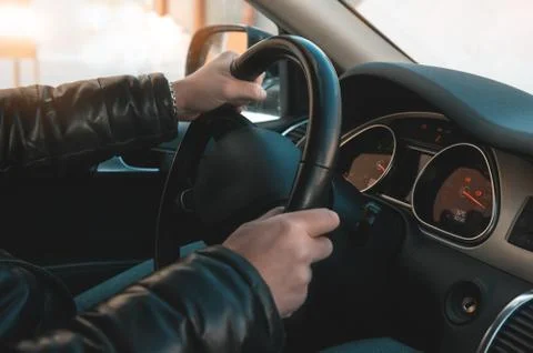A large man in a leather jacket and jeans sits behind the wheel of a car. Stock Photos