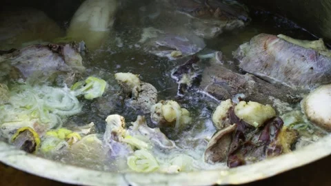 Large meat chunks boiling in broth in huge ancient cauldron for pilaf Stock Footage 346597961