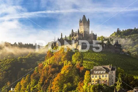 Large medieval castle on a colourful treed hillside with fog, blue sky and cloud Stock Photos