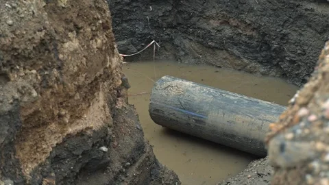 A large metal pipe rests in a muddy excavation surrounded by dirt. The site has Vidéo 344675895