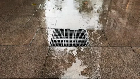 Large Metal Storm Drain Grate Flooded tiles Sidewalk during Tropical Rainstorm Stock Footage 343476915