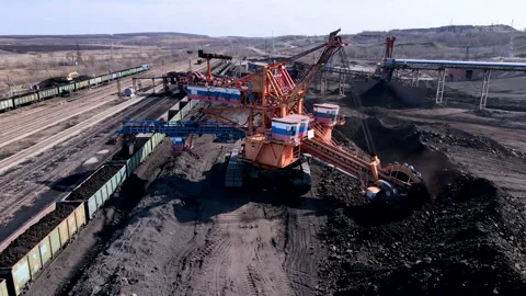 A large mining excavator picks up coal with a bucket and loads it onto a train. Stock Footage 152621949