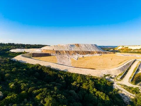 Large mining site with a high earth mound and surrounding greenery under a .. Stock Photos