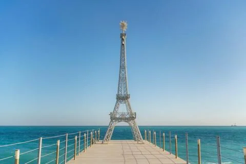 Large model of the Eiffel Tower on the beach. A woman walks along the pier Stock Photos