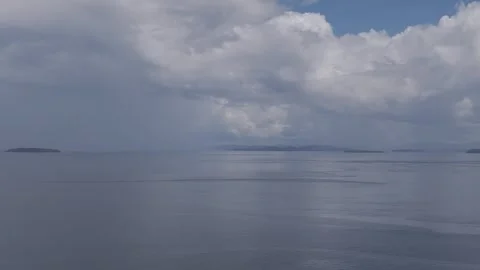 Large moody grey storm clouds over a calm seascape with small islands in Stock Footage 255371113