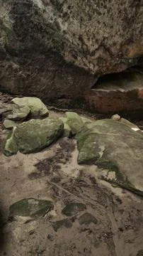 Large, moss-covered rocks sit beneath a sandstone overhang Stock Photos