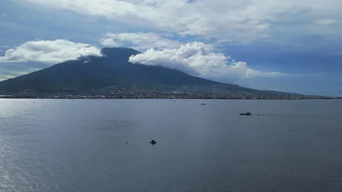 Large mountain rises above calm body of water under cloudy blue sky with boats Video stock 328045177
