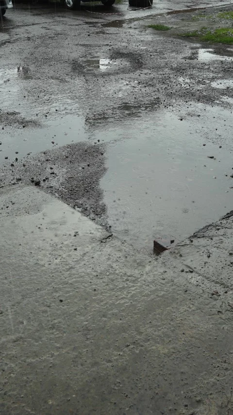 Large muddy water puddles on a damaged asphalt road during rain. Stock Footage 340334921