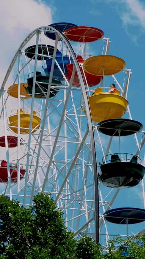 Large, multi-colored ferris wheel rotates against a blue and slightly cloudy sky Stock Footage 319780030