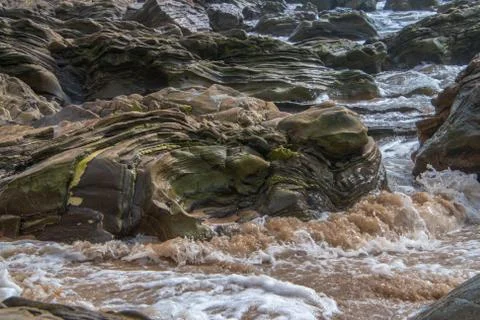 Large multi-layered boulder on beach with ocean waves hitting it as they appr Stock Photos