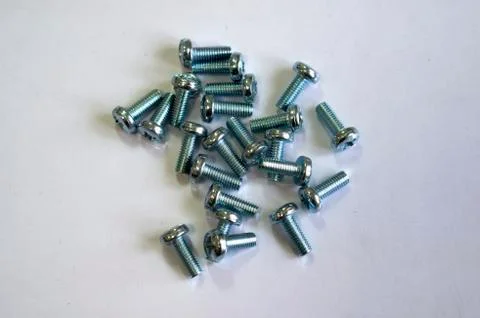 A large number of bolts on a white table. Fixing bolts. New bolts. Stock Photos