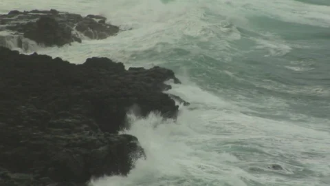 Large ocean tidal waves crash onto dark island rocks on shore Stock Footage 125340474