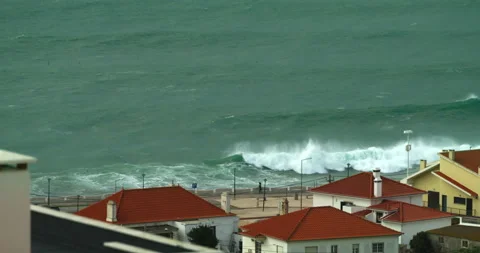 Large ocean waves roll onto a shore lined with white residential buildings with Stock Footage 220615823