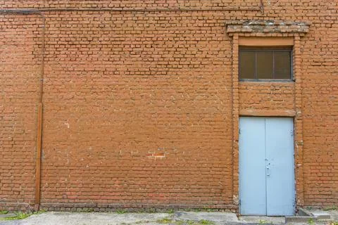 Large old dilapidated red brick house with a gray metal door. Old factory bui Stock Photos