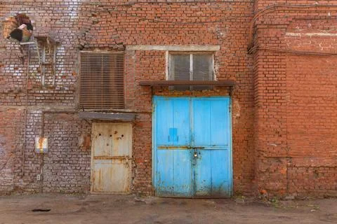 A large old dilapidated red brick house with large metal doors. Old dirty aba Stock Photos