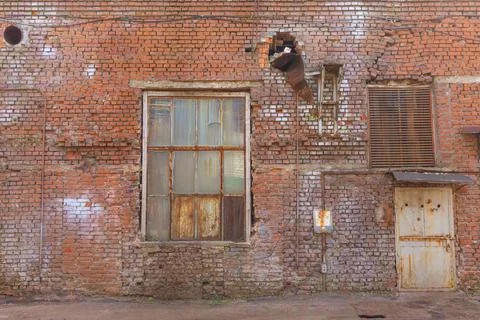 A large old dilapidated red brick house with a rusty window and a metal door. Stock Photos