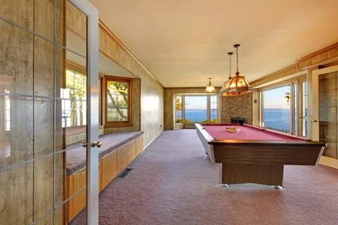 Large old room with pool table, window bench and water view. Stock Photos