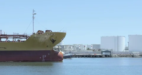 Large Old Tanker Ship Sails in Front of Petroleum Dock Stock Footage 129228712