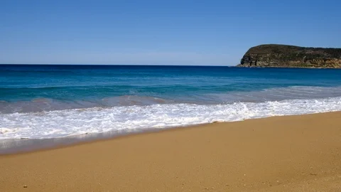 Large open beach with breaking waves onto clean beach with blue clear sky. Stock Footage 93723018