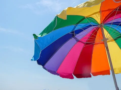 A large opened multi - colored beach umbrella against a blue sky Stock Photos