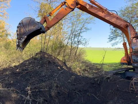 A large orange excavator is actively digging a sizeable hole in a field Stock Photos