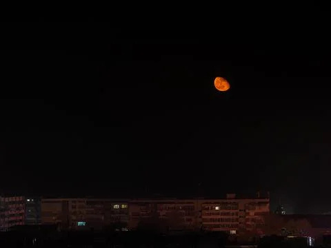 Large orange moon low in the sky over multi-storey residential buildins. Stock Photos