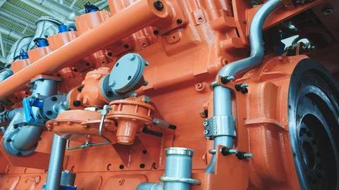 Large orange piston gas engine electric generator with many valves and pipes. Foto stock