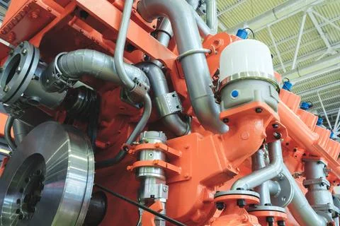 Large orange piston gas engine electric generator with many valves and pipes. Foto stock