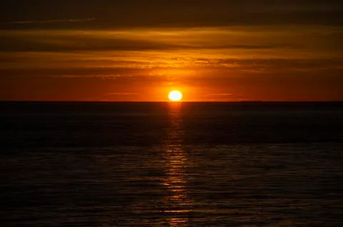 Large orange sunset as the massive sun sets into the horizon above the ocean, Stock Photos