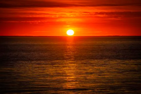 Large orange sunset as the massive sun sets into the horizon above the ocean, Stock Photos