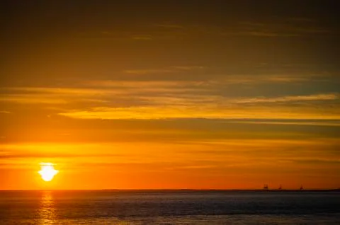 Large orange sunset as the massive sun sets into the horizon above the ocean, Stock-Fotos
