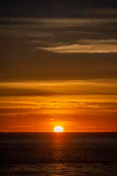 Large orange sunset as the massive sun sets into the horizon above the ocean, Stock-Fotos