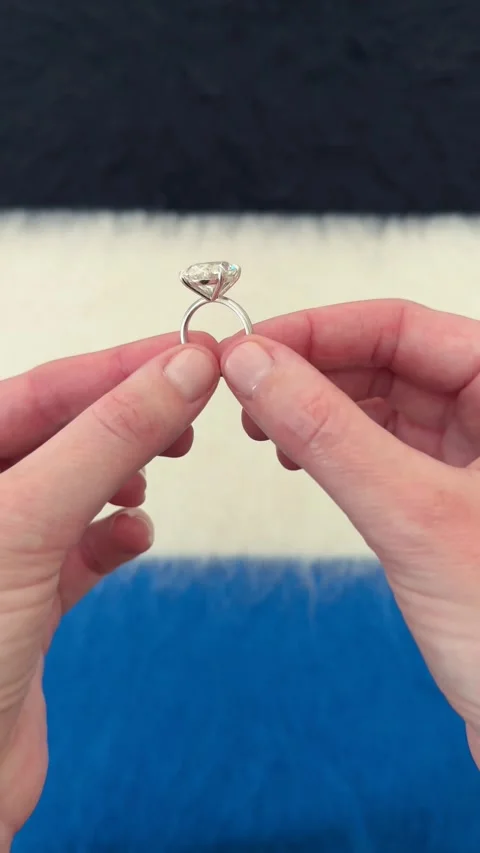 Large oval diamond engagement ring shown between hands blue backdrop Stock Footage 328251271