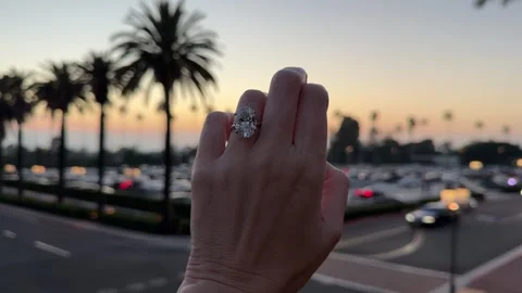 Large oval diamond solitaire engagement ring on hand with palm trees 스톡 동영상 325876460