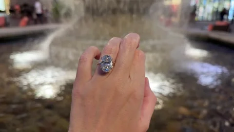 Large oval diamond solitaire engagement ring on hand with flowing water fountain Stock Footage 325876694