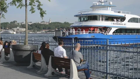 Large passenger ferry docking at Karakoy docks with people sitting in foreground Stock Footage 90710238