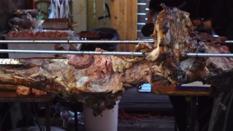 A large piece of meat carcass on a spit rotates grilling Stock Footage 128114179