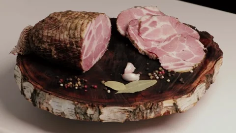 A large piece of pork ham and sliced ham rotate on a kraft wooden board Stock Footage 262191505